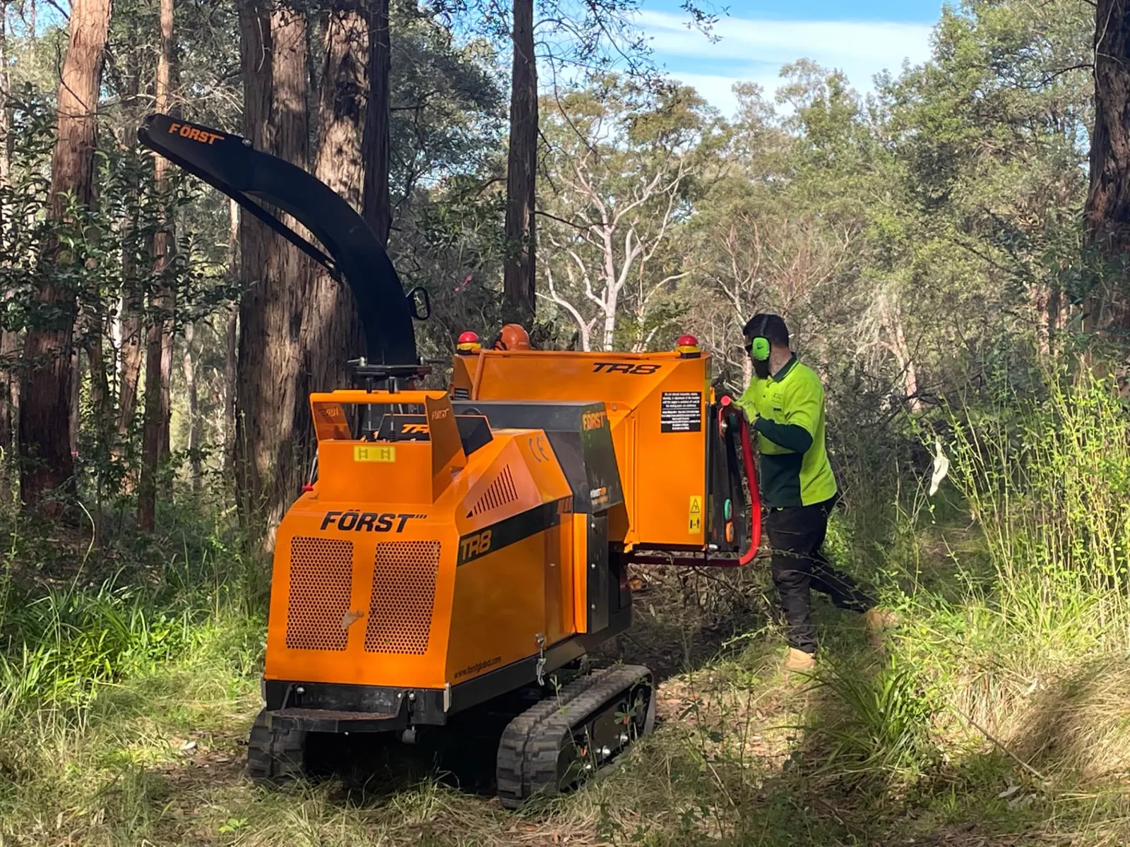 Arborist feeding limbs into a tracked chipper in bushland