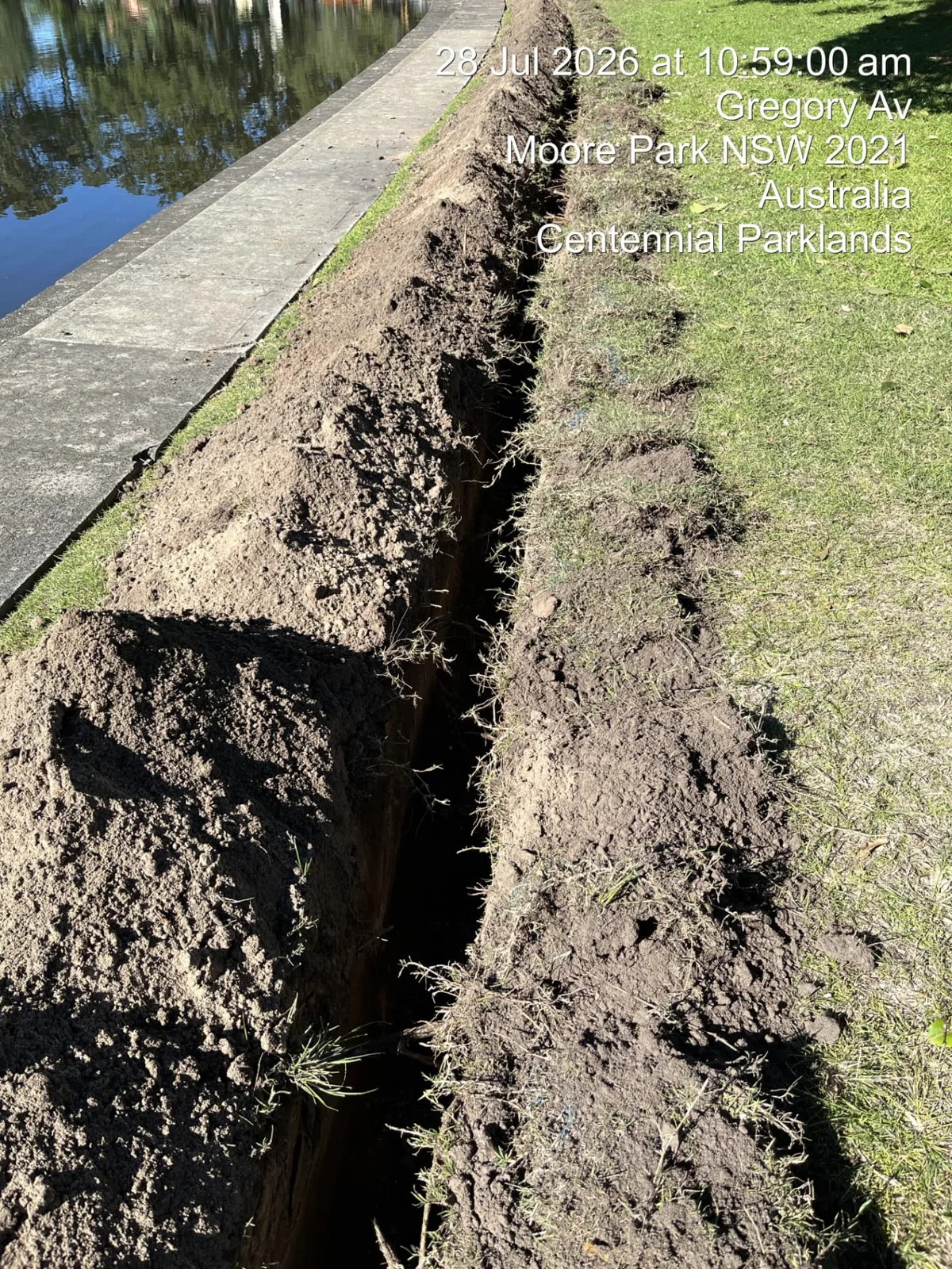 Narrow trench excavated beside a pond edge path in Centennial Parklands