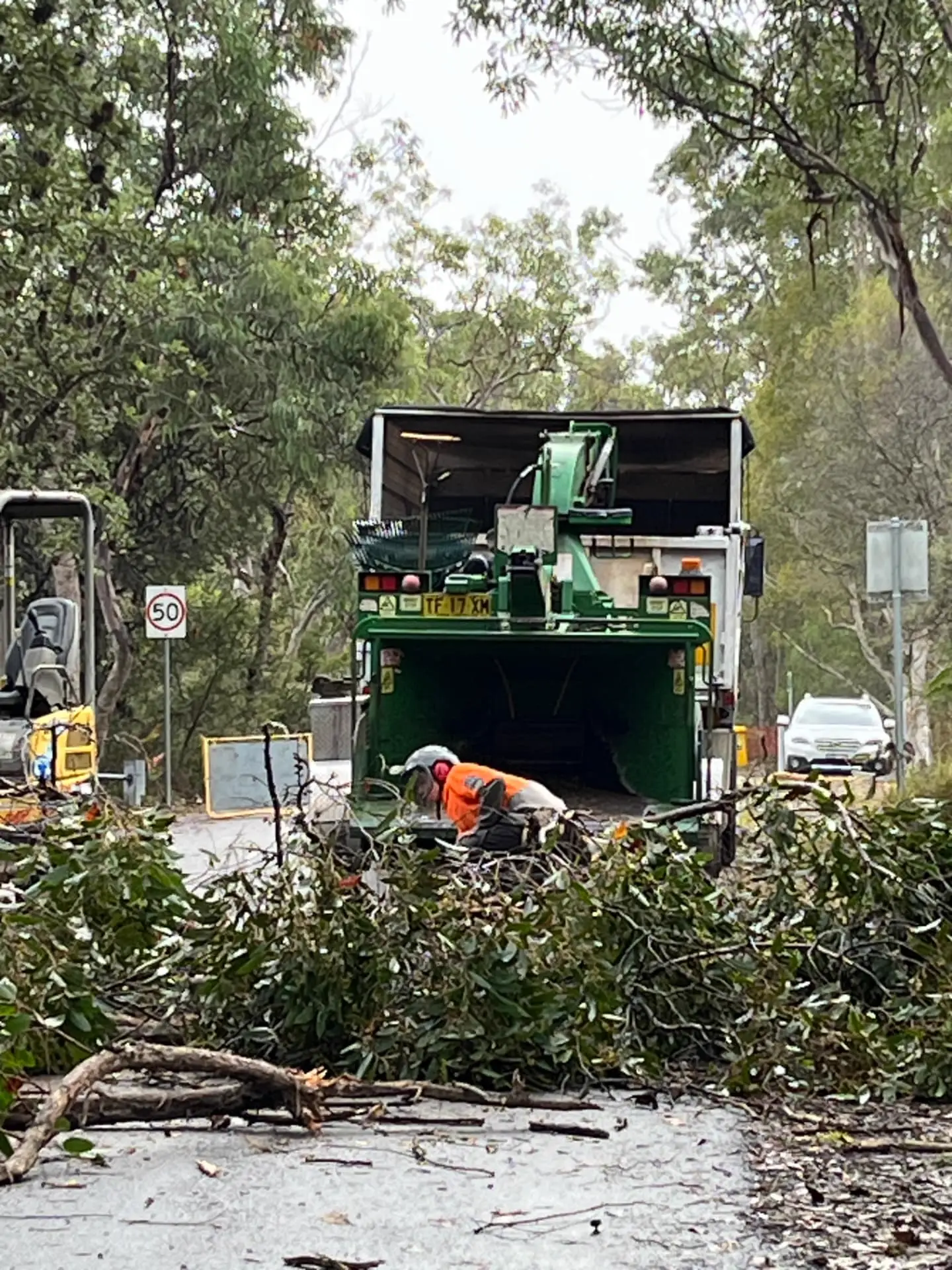 Arborist feeding branches into a wood chipper on a bush road